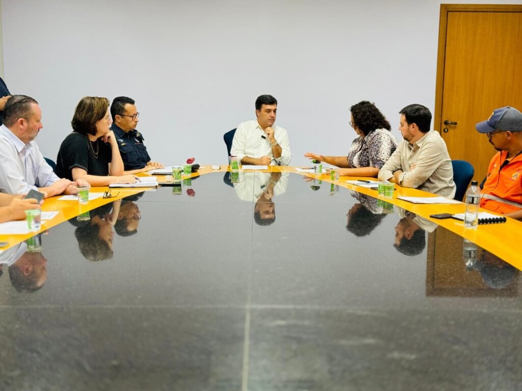 A imagem mostra a sala do Gabinete, com uma mesa de reunião em granito preto com bordas em madeira clara, o prefeito Dr. Custódio está sentado na ponta e aos lados estão os outros participantes da reunião