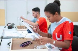 Dois jovens, uma menina e um menino, com uniforme vermelho da Fiec, olhando para tablets e estudando.